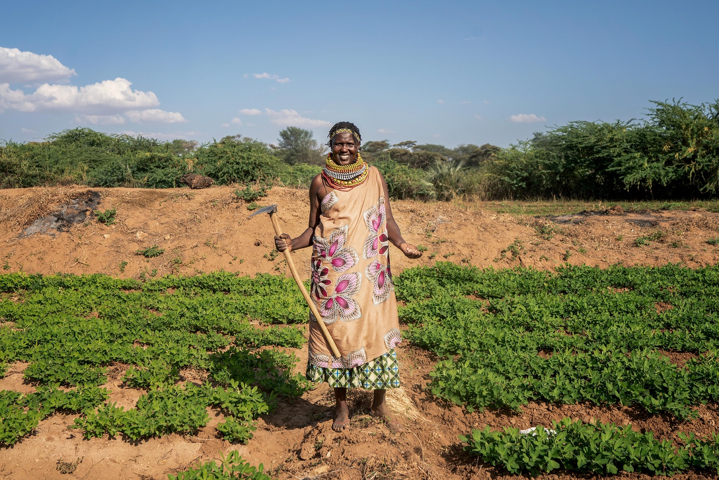 A female farmer stands in a field holding a farming tool