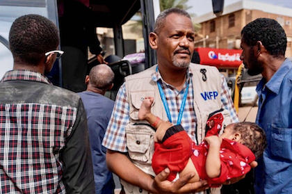 Man standing up in WFP vest, holding a baby