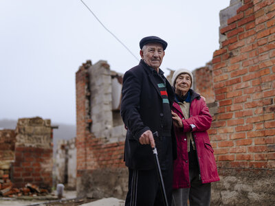An elderly man and woman standing in front of a building structure