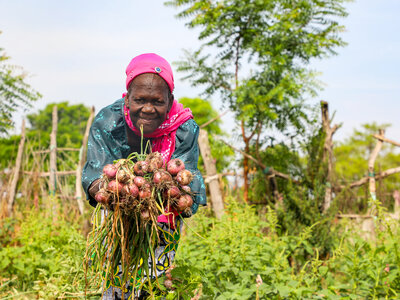 A smiling farmer working in a green field shows her harvest in her hands
