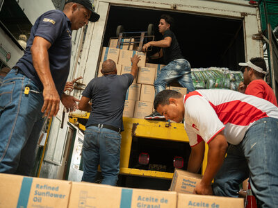 Workers unload boxes of fortified sunflower oil from the back of a truck, forming a chain to move food supplies during a distribution operation in Venezuela.