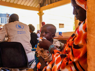 Copilot said:  A child receives nutritional support at a WFP clinic as caregivers and health workers gather during a community health and nutrition session.