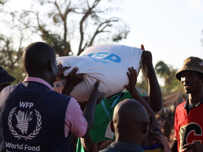 A WFP staffer is holding a sack of WFP food along with another man whose face is obscured by the sack.