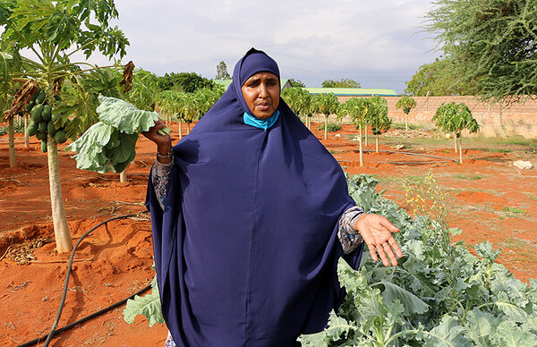 Habiba poses for pictures with leafy greens on her farm