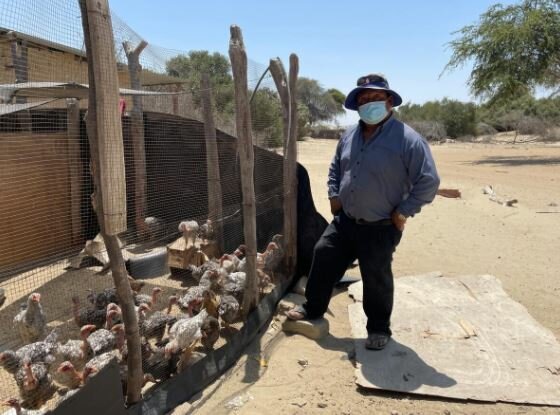 Maria's husband stands next to their chicken barn.