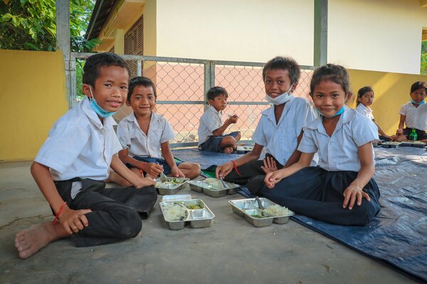 A group of children sit on the ground and eat lunch