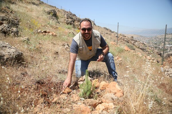 A WFP staff member kneels on the ground in front of some crops