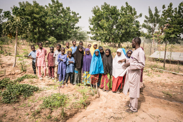 A teacher and his students stand next to their school garden
