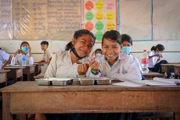 Two smiling girls eat lunch together in a classroom