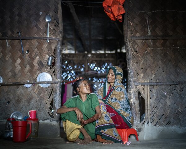 A woman and her son sit in the doorway of their house and smile at each other