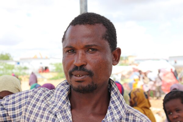 A Somali man in  a checkered shirt looks into camera