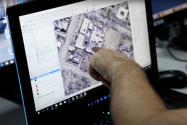 Finger pointing at computer screen showing aerial images.