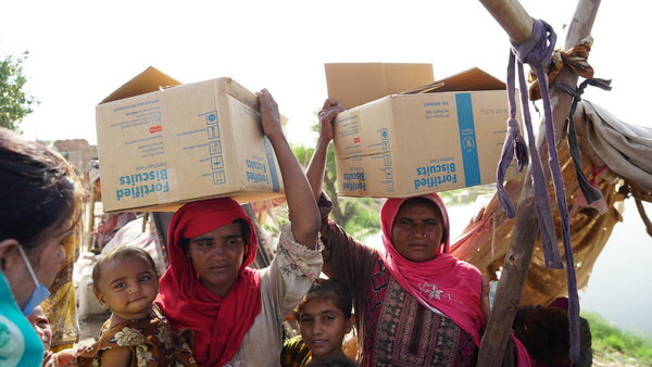 Two women carry boxes marked 'Fortified biscuits' on their heads