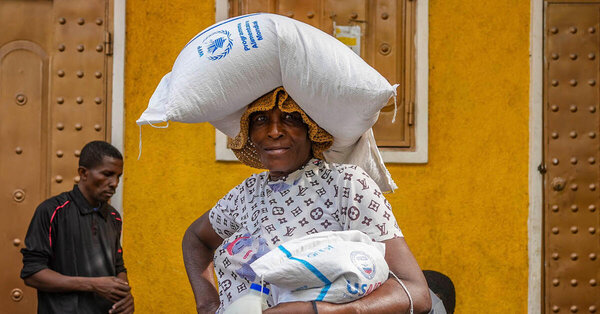 A woman balances a large white WFP food bag on her head. Photo: WFP/Luc Junior Segur