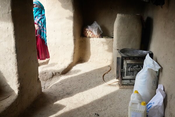 Containers of WFP food and vegetable oil sit on the ground of a bare room, as a woman in traditional Afghan dress walks outside. 