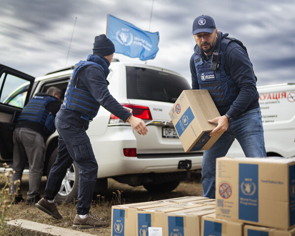 WFP staff unload food boxes from vehicles in an open field, preparing emergency supplies for delivery to communities affected by the crisis.