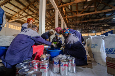 WFP staff package food aid in a warehouse, sorting canned goods and supplies into containers to support vulnerable communities ahead of crisis conditions.
