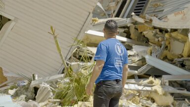 A man with a blue WFP T-shirt surveys damaged buildings. Photo: WFP/Gustavo Vera