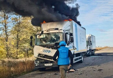 A man in a blue vest and matching cap rushes to a burning and smashed WFP truck. Photo: WFP