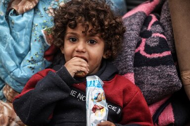 © WFP/Ali Jadallah A little child with curly hair eating a biscuit provided by WFP.