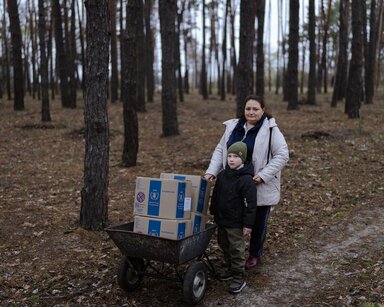 Natalia’s Life, Twenty Kilometres from the Frontline, standing in the forrst with WFP food parcels