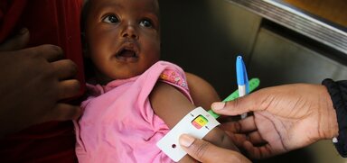 A little girl being tested for malnutrition with Mid Upper Arm Circumference test (MUAC) and receiving special fortified food from WFP at a WFP-supported clinic in North Kordofan.