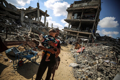 A man holds a child as he cries amid a scene of destroyed buildings in Gaza