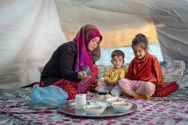A mother and her children are having their food in a tent