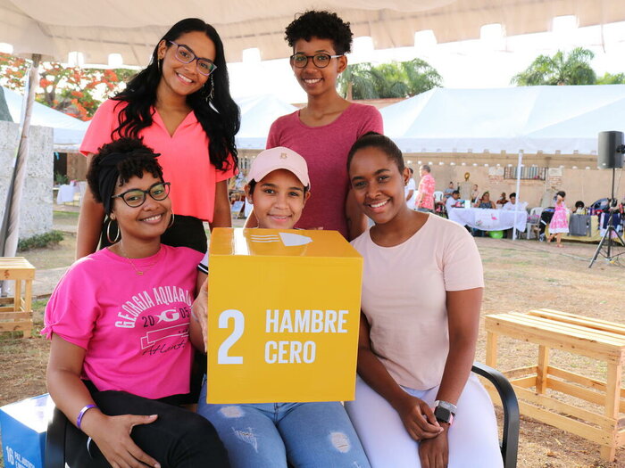A group of five young women hold the Sustainable Development Goal 2 (SDG 2) logo during the Zero Hunger Movement stand, during Zone Food Fest.