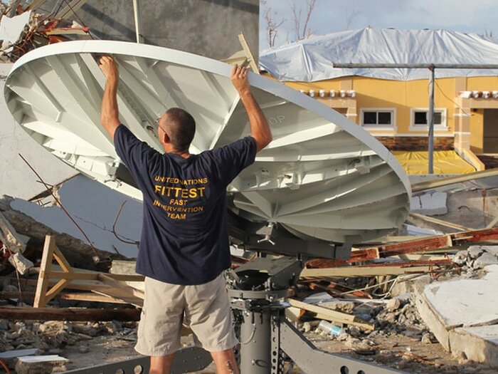 WFP staff setting up satellite dish among rubble