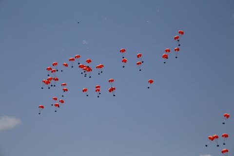 Orange parachutes rain down from a blue sky