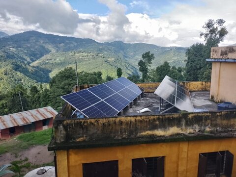 Rooftop solar panels with a scenic view of green hills and a cloudy sky, highlighting sustainable energy in a natural landscape..