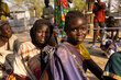 Three girls look into the camera with gentle smiles as they wait sat on the ground a food aid registration in south sudan