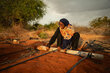A women in a grey hijab and colourful scarf fixes an irrigation pipe on her land. Photo: WFP/Arete/Edwin Ndeke