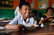 A grinning school boy tucks into a bowl of fortified rice at class. Photo: WFP/Darapech Chea