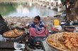 A woman in a long skirt and blue sits on the ground, stirring fritters she is cooking at her makeshift stall. Photo: WFP/Htet Oo Linn