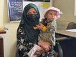 A woman in a face-covering headscarf holds her baby daughter who wears a frilly pink bonnet. Photo: WFP/Danijela Milic