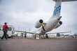 A person heads to a white plane with a WFP logo on it, with boxes piled upon the tarmac waiting to be loaded. Photo: WFP/Michael Castofas