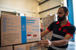 Warehouse worker handles WFP “Fortified Biscuits” carton, stacking boxes inside a warehouse with pallets of food aid supplies visible in the background.