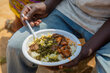 A closeup of a man's hands holding a bowl of food. Photo: WFP/Arete/Seros Muyisa