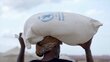 A closeup shot of a man with a turban carrying a large white bag of WFP food on his head. Photo: WFP
