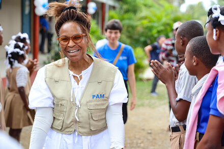 A smiling woman with a tan WFP vest, backdropped by kids 