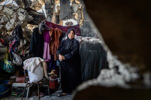 A woman in a black gown and headscarf stands in a heavily war-damaged building surrounded by clothes and other basic belongings. Photo: WFP/Maxime Le Lijour