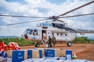 WFP UNHAS helicopter on a dirt airstrip in eastern DRC as responders load supplies, with boxes of protective equipment in the foreground.