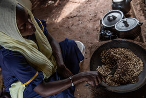 A woman in a yellow headscarf cooks grains inside a dark room. Photo: WFP/Gabriela Vivacqua