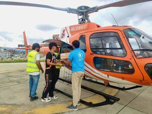 A WFP staffer hands over boxes to two workers for loading onto an orange helicopter for Nepal's flood response. Photo: WFP/Shraddha Bhattarai