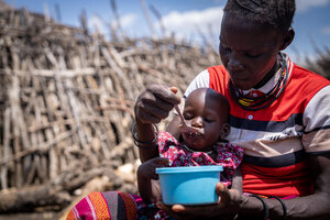 A mother sits outside feeding her little girl out of a blue bowl. Photo: WFP/Daisy Masembe