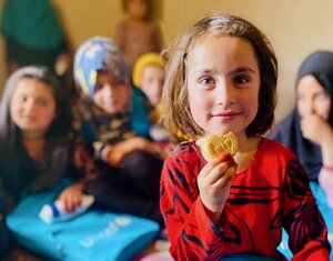 A smiling Afghan primary school girl holds up a WFP fortified biscuit. Photo: WFP/Sayed Abidullah Sadat