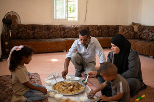 A West Bank family gathers inside around a large plate of food on the floor, sharing it in traditional style. Photo: WFP/Hugh Rutherford