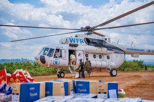 People unload WFP food boxes and other supplies from a WFP-managed UNHAS helicopter parked in a dirt landing site. Photo: WFP/Michael Castofas